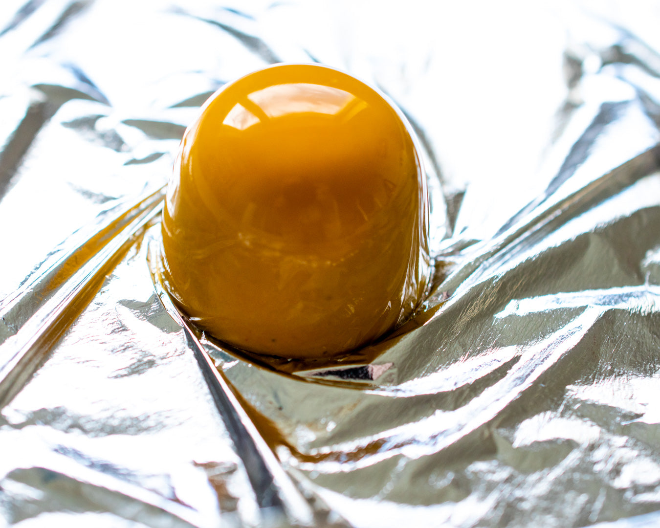 A glossy amber Irish chocolate bonbon on foil, handmade wedding favours and gifts for guests.